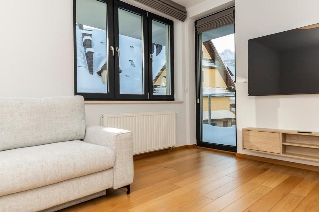 Ein modernes Wohnzimmer mit einer Couch, einem großen Fenster, einem Fernseher und einer Schiebeglastür.