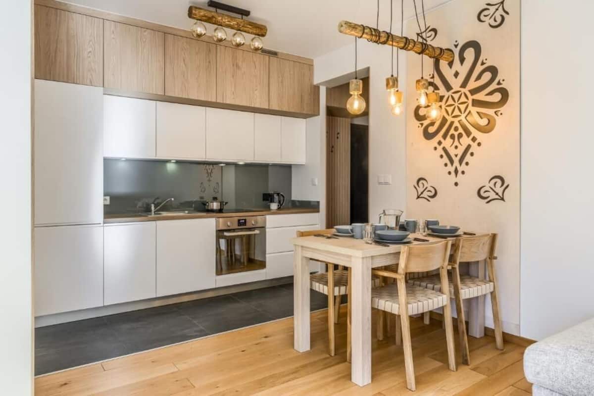 Una cocina moderna con armarios blancos, una mesa de comedor con sillas y un elemento decorativo en la pared.