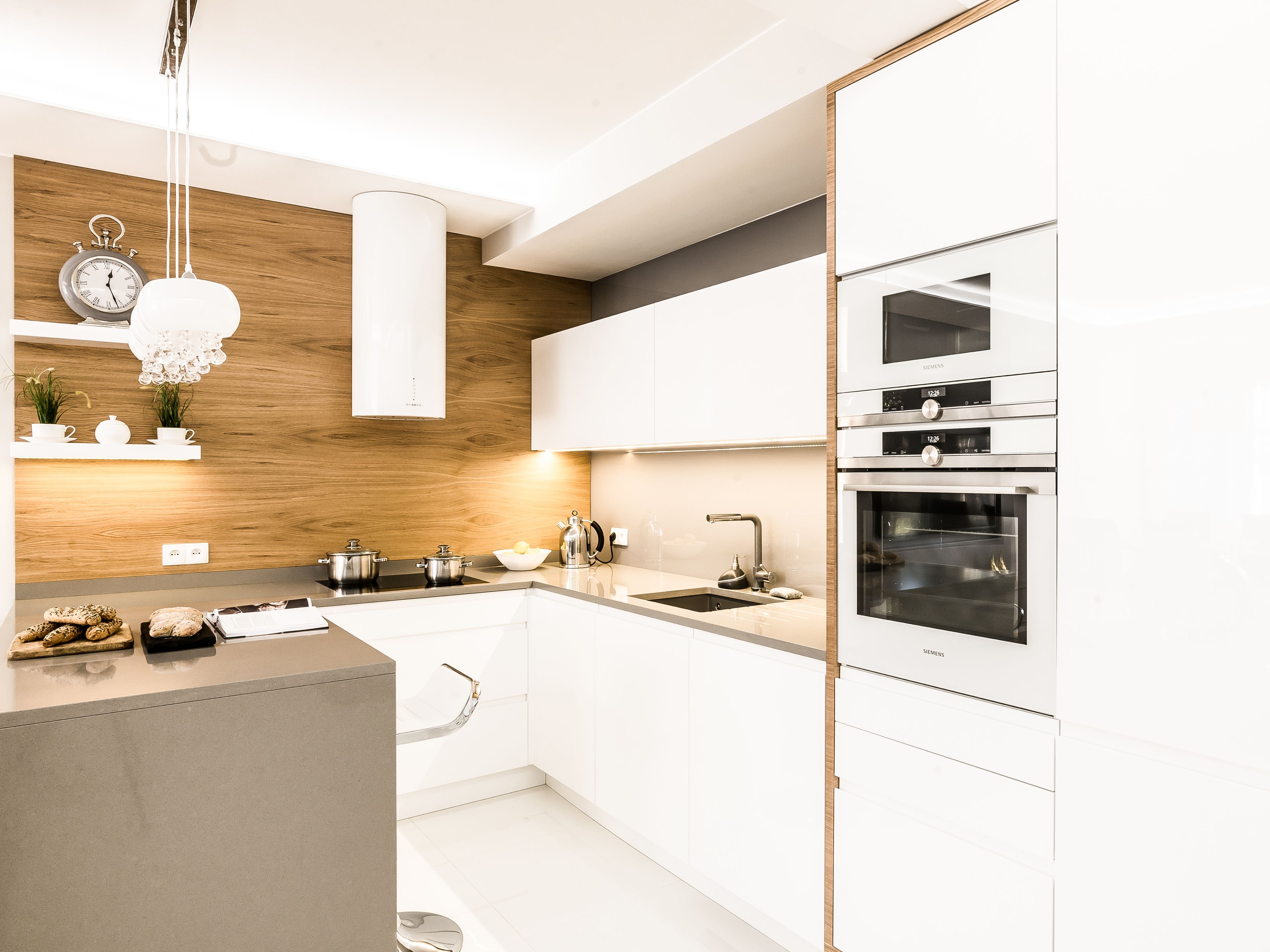 Una cocina moderna con armarios blancos, horno empotrado y una pared de acento de madera.