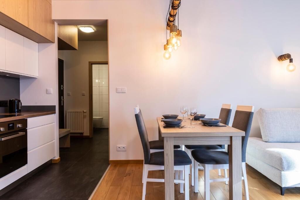 A modern kitchen with white cabinets, a dining table with chairs, and a light fixture above.