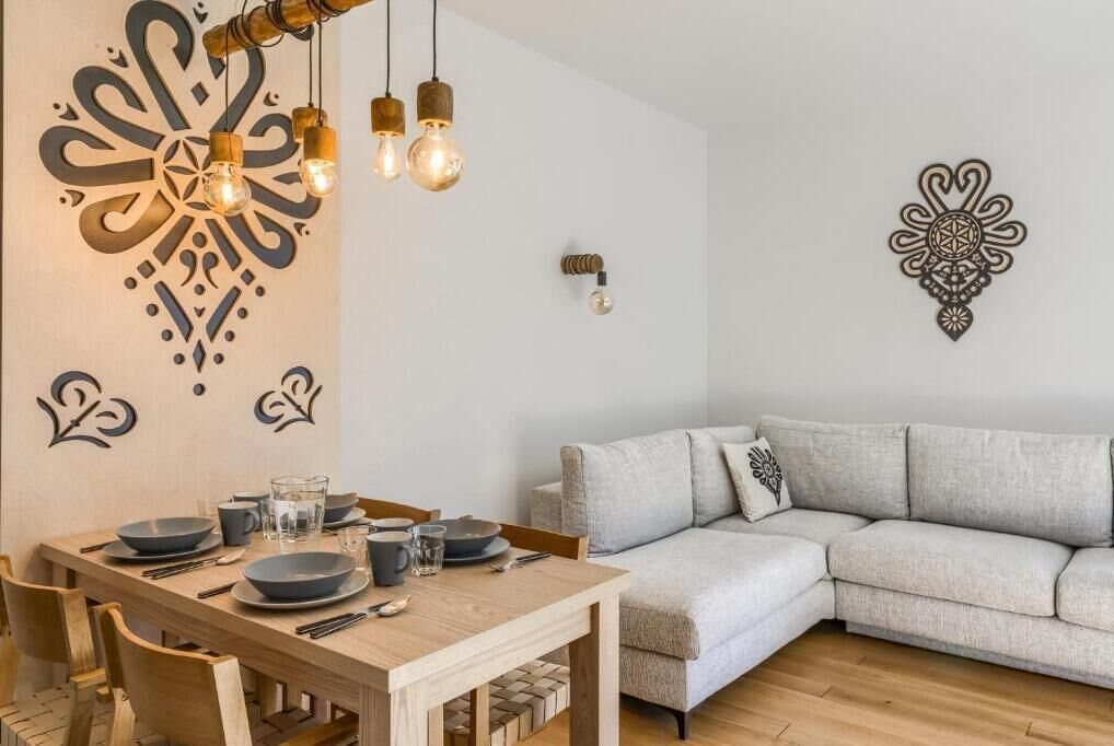 A dining area with a wooden table set for four, a grey sofa, and wall decor.