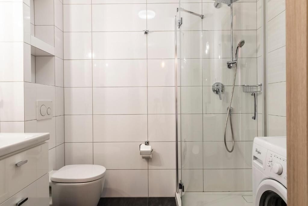 Een moderne badkamer met toilet, een douchecabine van glas en een wasmachine.