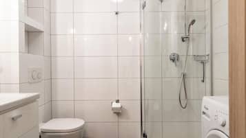 A modern bathroom with a toilet, a glass-enclosed shower, and a washing machine.