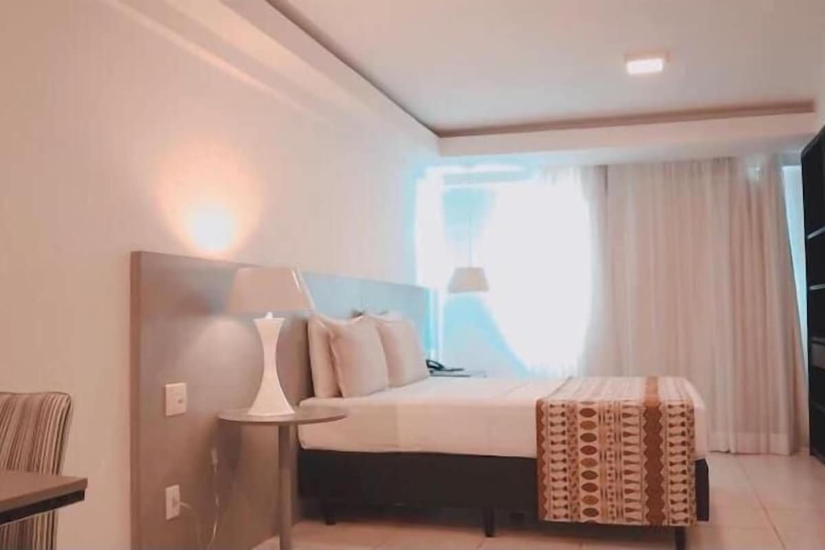 Une chambre d’hôtel avec un lit, une table de chevet, une lampe et une vue sur l’extérieur.