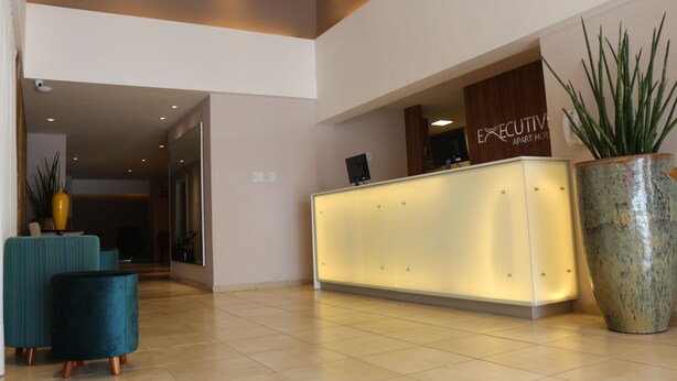 A reception area with a modern reception desk, a large potted plant, and teal upholstered chairs.