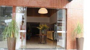 A hotel entrance with a glass door, a reception desk, and potted plants.