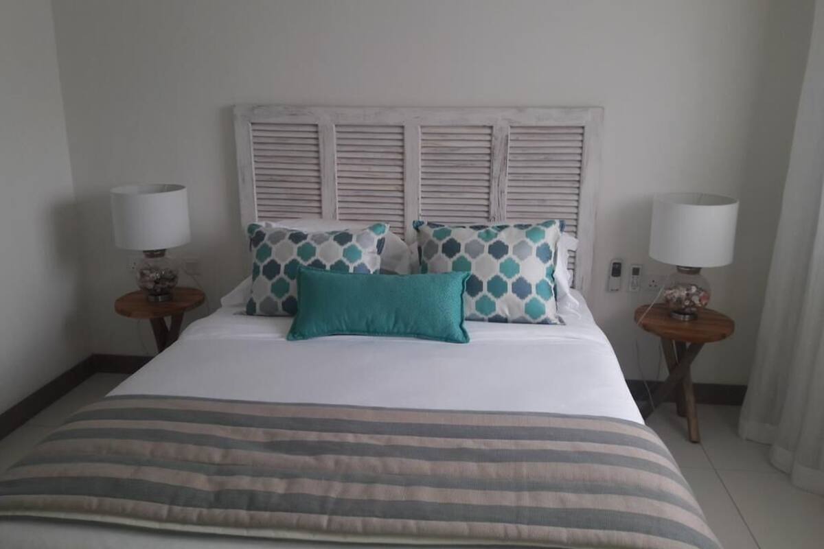 A neatly made bed with a striped bedspread, two matching pillows, and a white headboard. There are two bedside tables with lamps and a small decorative item on each.
