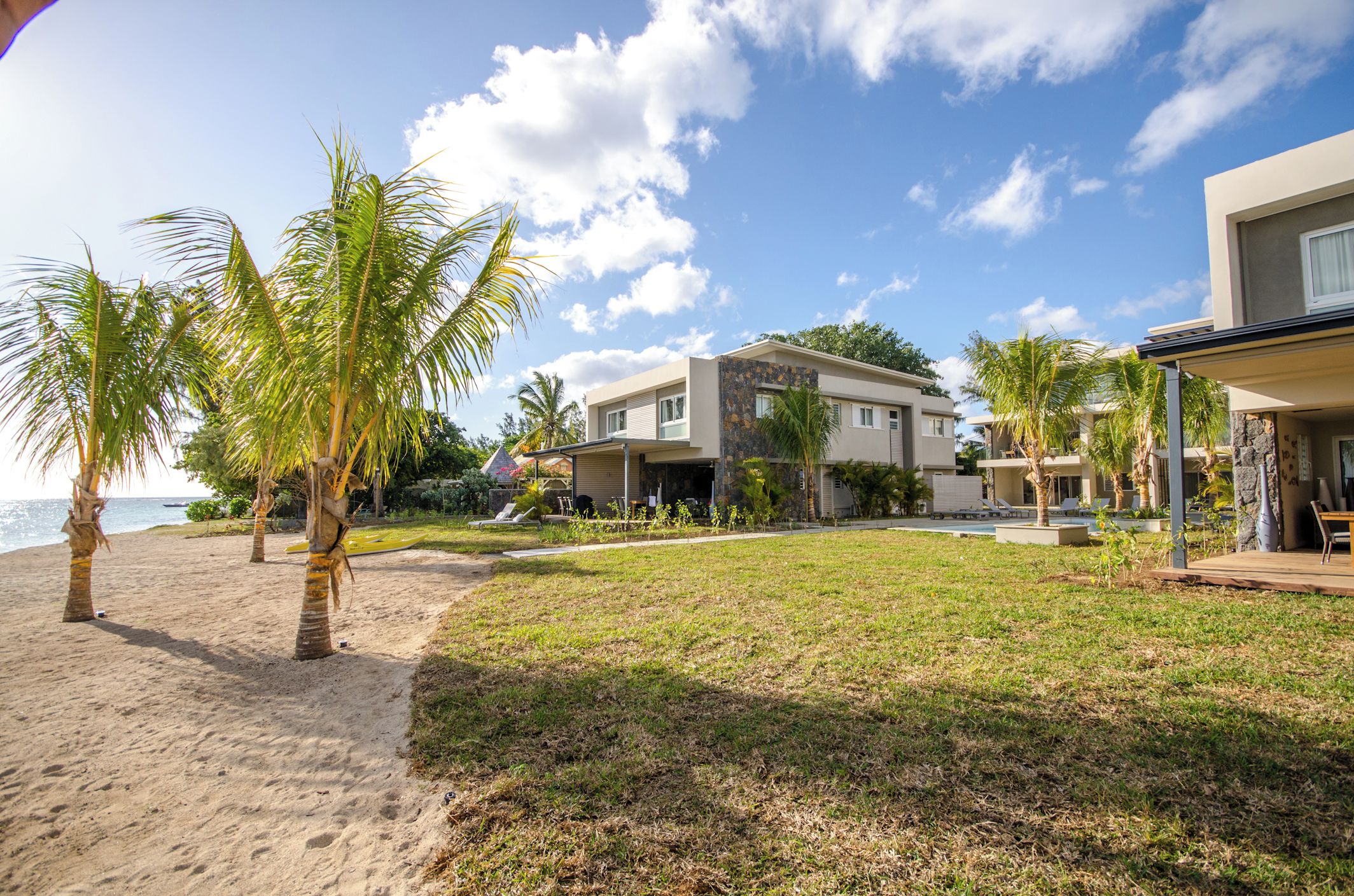 A beachfront property with modern architecture, a grassy lawn, and palm trees.