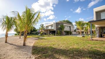 A beachfront property with modern architecture, a grassy lawn, and palm trees.