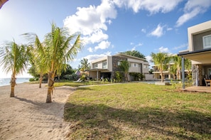 A beachfront property with modern architecture, a grassy lawn, and palm trees. - L'escale Beachfront Luxury Suite By Dream Escapes (Black River)