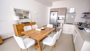 A modern kitchen with a wooden dining table, white chairs, and stainless steel appliances. - L'escale Beachfront Luxury Suite By Dream Escapes (Black River)