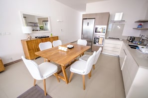 A modern kitchen with a wooden dining table, white chairs, and stainless steel appliances. - L'escale Beachfront Luxury Suite By Dream Escapes (Black River)