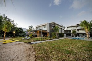 A modern hotel with a pool, outdoor seating, and a well-maintained lawn. - L'escale Beachfront Luxury Suite By Dream Escapes (Black River)