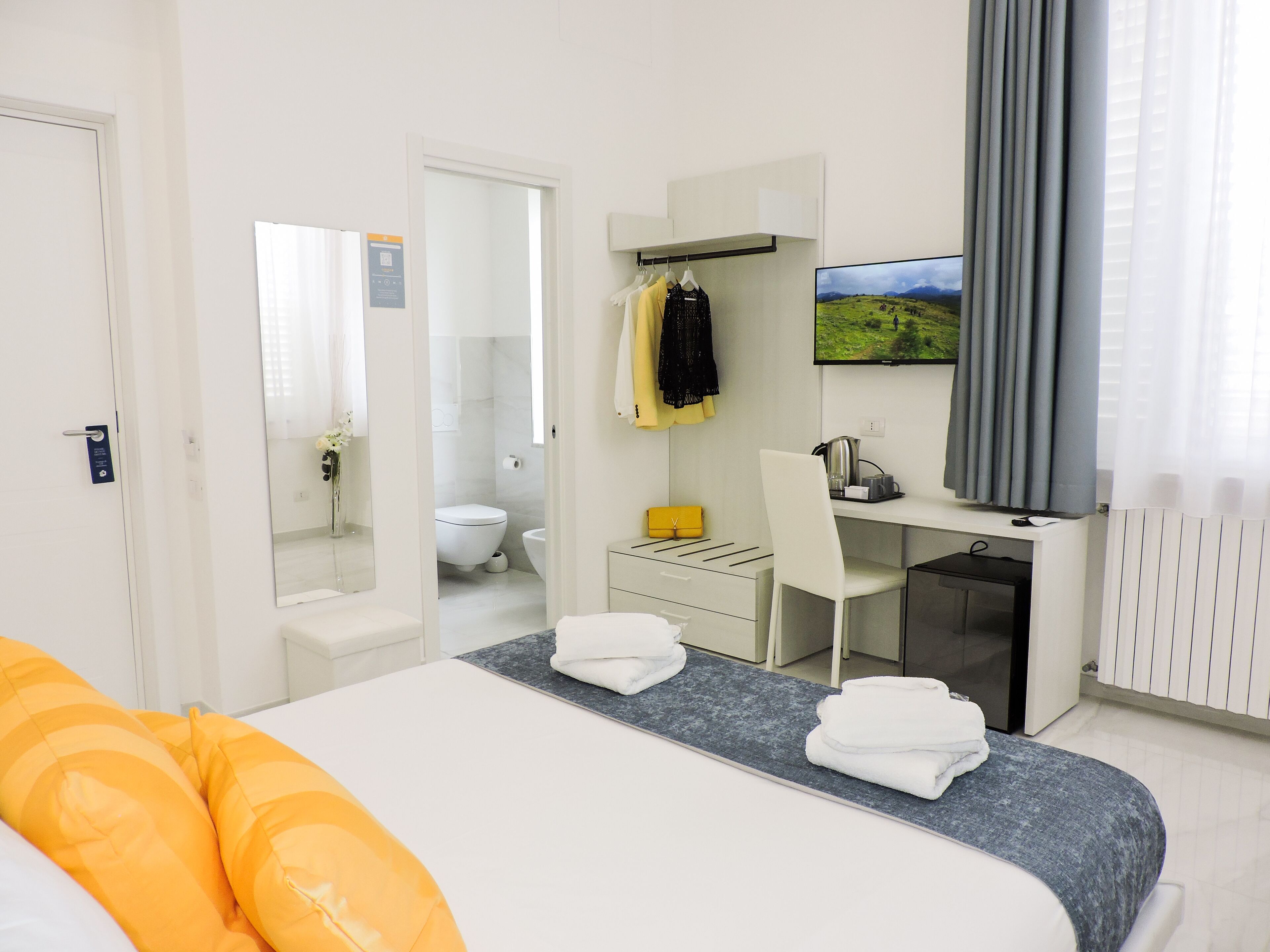A modern hotel room with a bed, a desk, a chair, a TV, and a bathroom visible through an open door.