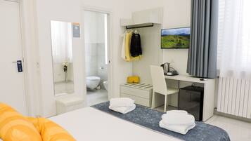 A modern hotel room with a bed, a desk, a chair, a TV, and a bathroom visible through an open door.