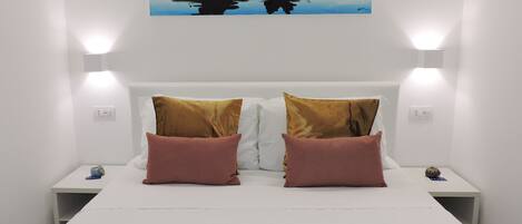 A hotel room with a bed, two pillows, a painting, and a nightstand with a lamp.
