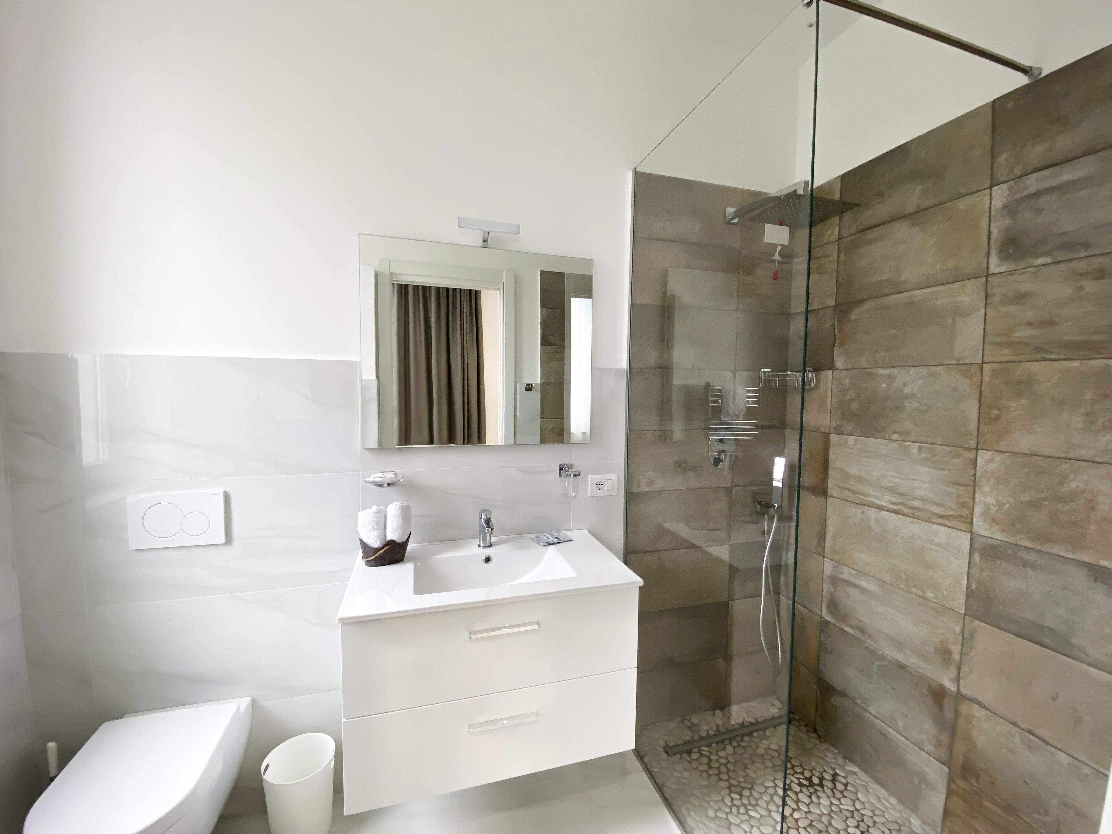 A modern bathroom with a glass-enclosed shower, a white sink with a mirror above, and a white vanity with drawers.