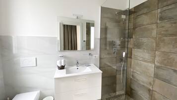 A modern bathroom with a glass-enclosed shower, a white sink with a mirror above, and a white vanity with drawers.