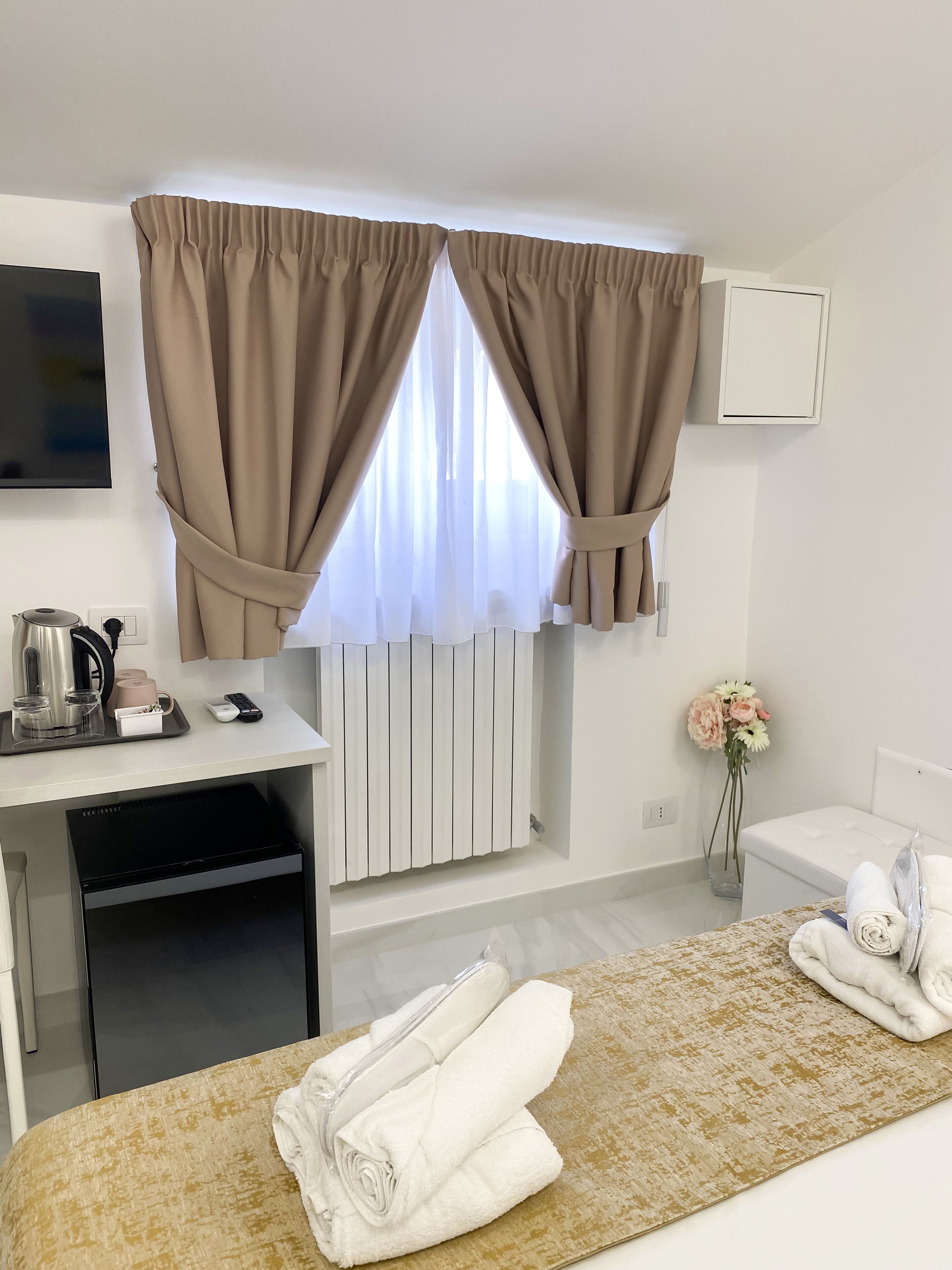 Una habitación de hotel con una cama, un escritorio con hervidor, un control remoto y un florero con flores.