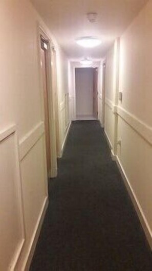 Un pasillo estrecho alfombrado, con paredes y puertas blancas a ambos lados.