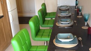 Un espace repas avec une longue table, des chaises à revêtement vert et un comptoir noir.