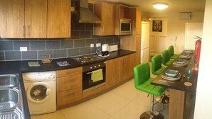 Une cuisine avec des meubles en bois, un évier en acier inoxydable, un lave-linge et un coin bar avec des chaises vertes.