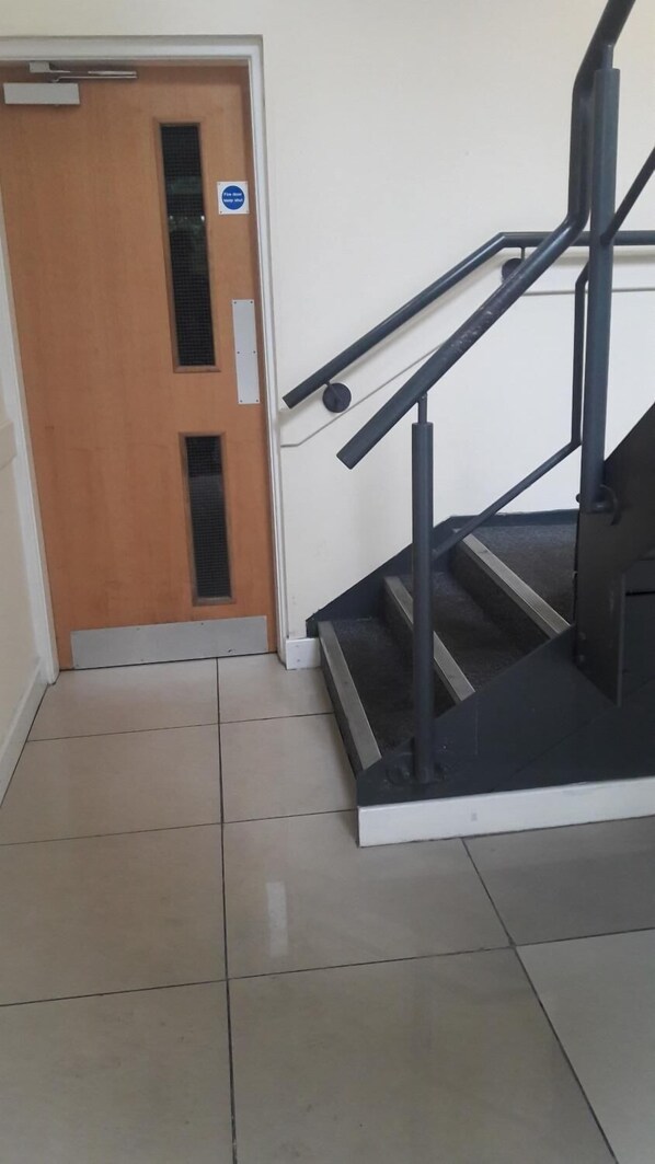 A staircase with metal railings and a wooden door with a vent. - Alton Apartments (Bradford)