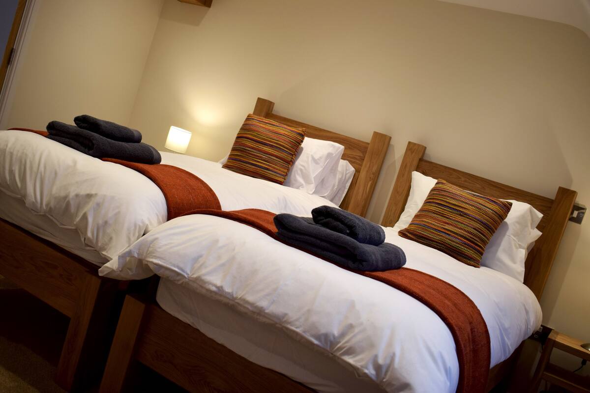 A hotel room with two beds, each with white linens, brown headboards, and a single bedside lamp.