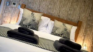A neatly made bed with a wooden headboard, two pillows with a rabbit design, and a woven blanket. - The Horse & Jockey Wessington (Alfreton)