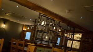 A dining area with wooden chairs and tables, a central light fixture with exposed bulbs, and a brick wall in the background. - The Horse & Jockey Wessington (Alfreton)