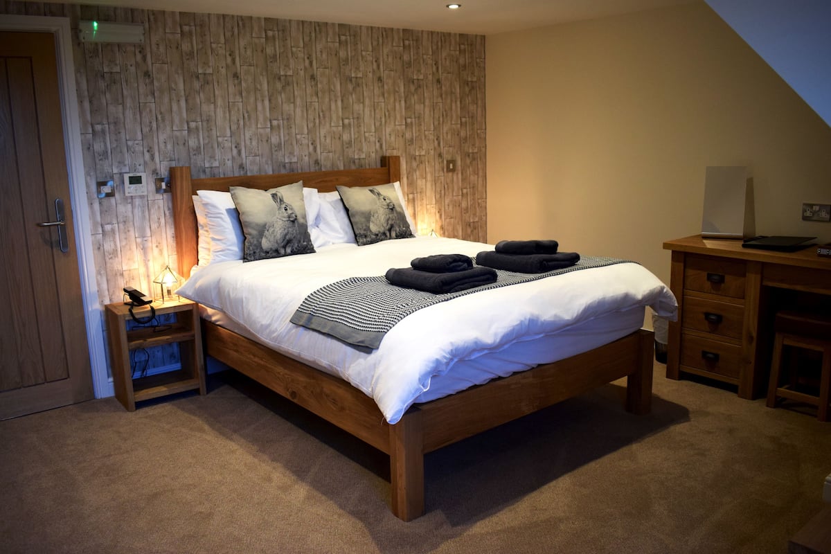 A bedroom with a wooden bed, white bedding, and a nightstand with a lamp.