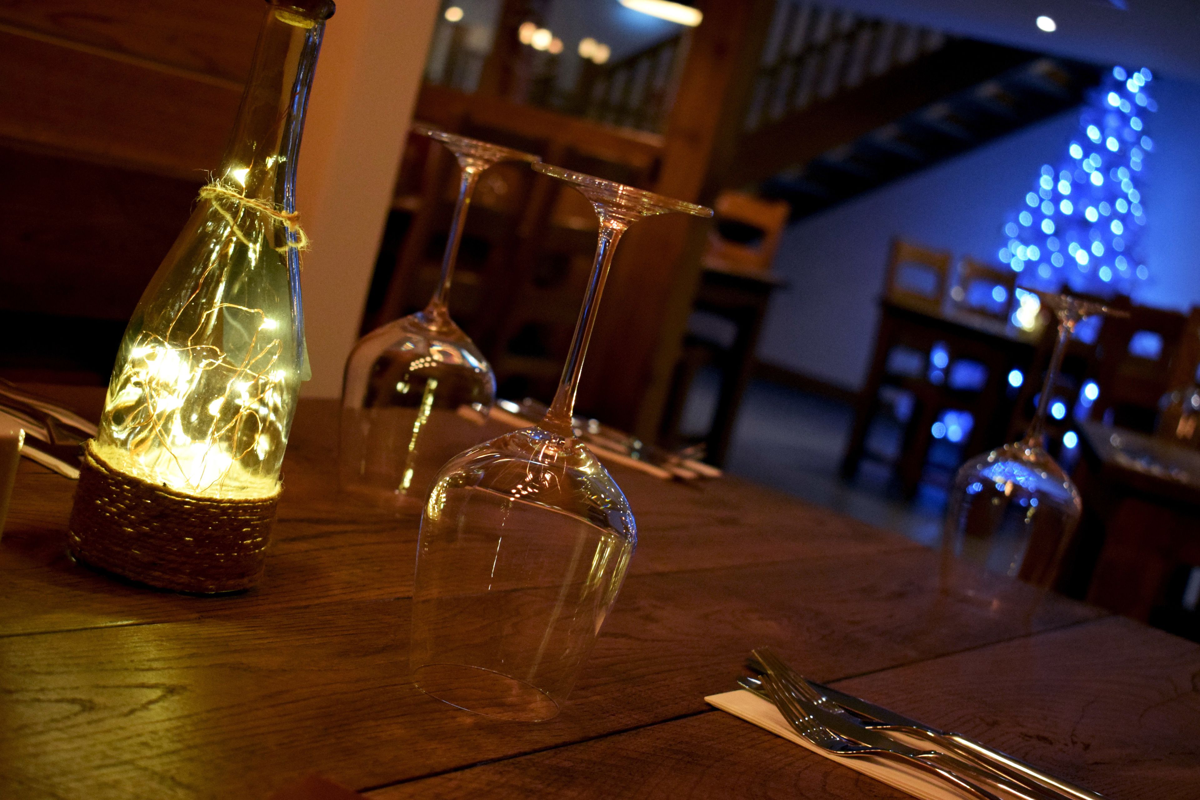 A wooden table with wine glasses and a bottle, lit by string lights.