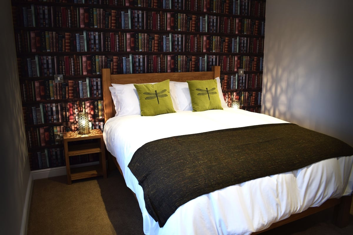 A neatly made bed with a wooden headboard, two pillows, and a green throw blanket.