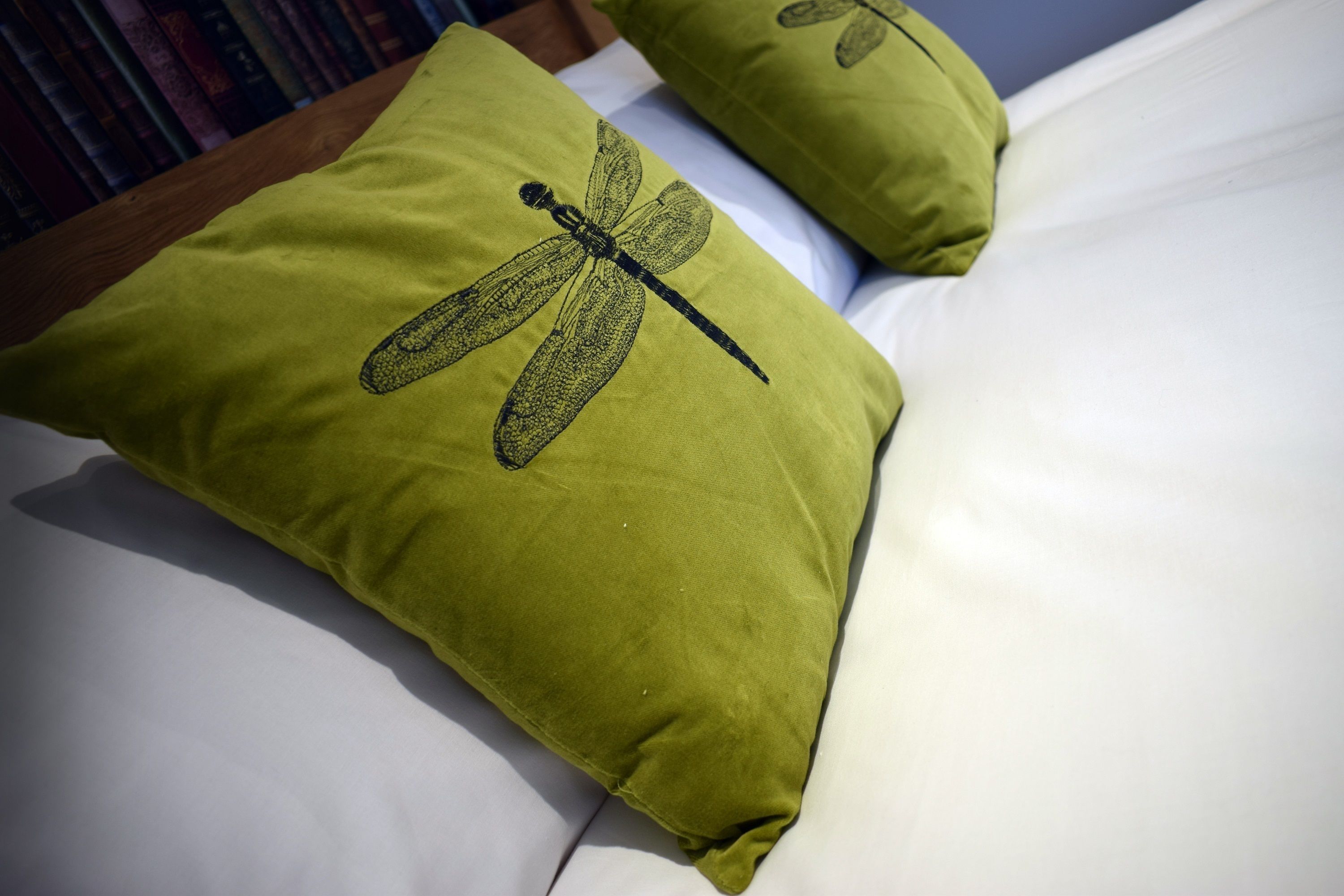 A bed with two pillows, one featuring a dragonfly design.