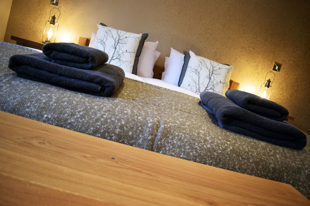 A neatly made bed with folded towels, a wooden headboard, and wall-mounted lamps.