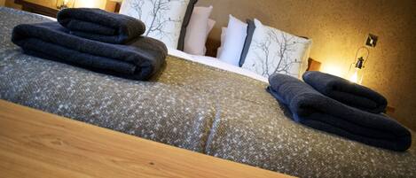 A neatly made bed with folded towels, a wooden headboard, and wall-mounted lamps.