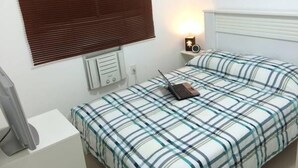 A bedroom with a bed, a bedside table, a lamp, a wall-mounted heater, and a picture frame. - Apartamento Barra da Tijuca (Rio de Janeiro)