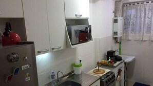 A compact kitchen with a refrigerator, stove, sink, and a small countertop. - Apartamento Barra da Tijuca (Rio de Janeiro)