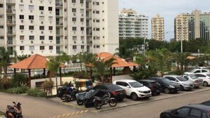 A parking area with multiple cars and motorcycles, a building with balconies, and a clear sky. - Apartamento Barra da Tijuca (Rio de Janeiro)