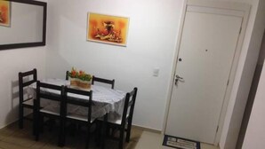 A dining area with a table and chairs, a door, and a small rug. - Apartamento Barra da Tijuca (Rio de Janeiro)