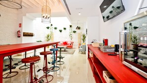Un área de bar moderna con taburetes rojos, una barra larga de color rojo y un televisor montado en la pared.