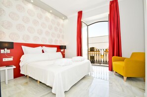 Quarto de hotel com cama grande, mesa de cabeceira, poltrona amarela e varanda com cortinas vermelhas.
