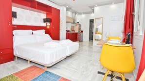 Una habitación de hotel moderna con una cama grande, una pequeña mesa con una silla, y un baño a la vista al fondo.