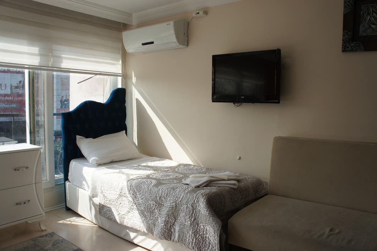 Ein Schlafzimmer mit einem Bett, einem an der Wand montierten Fernseher, einem Fenster mit Jalousien und einer Klimaanlage.