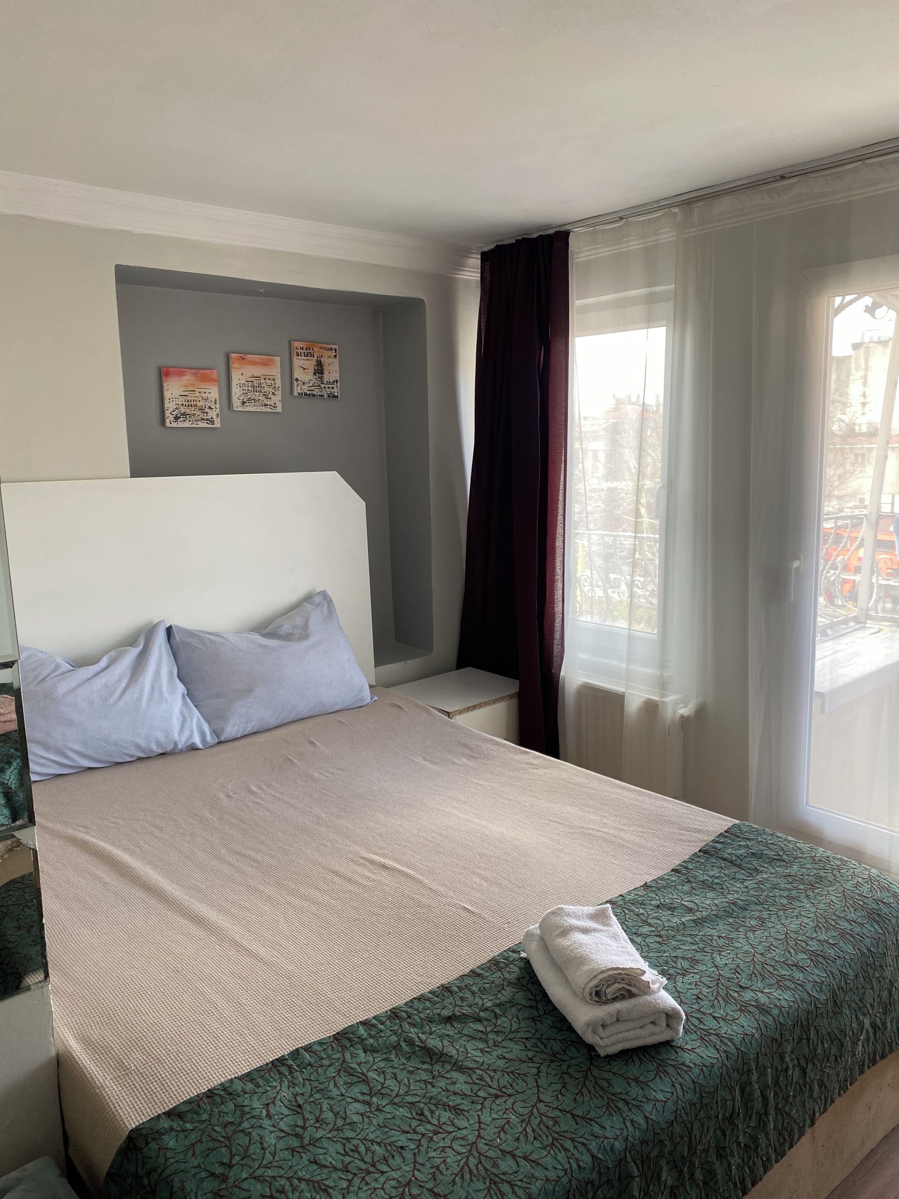 A hotel room with a bed, a window with curtains, and artwork on the wall.