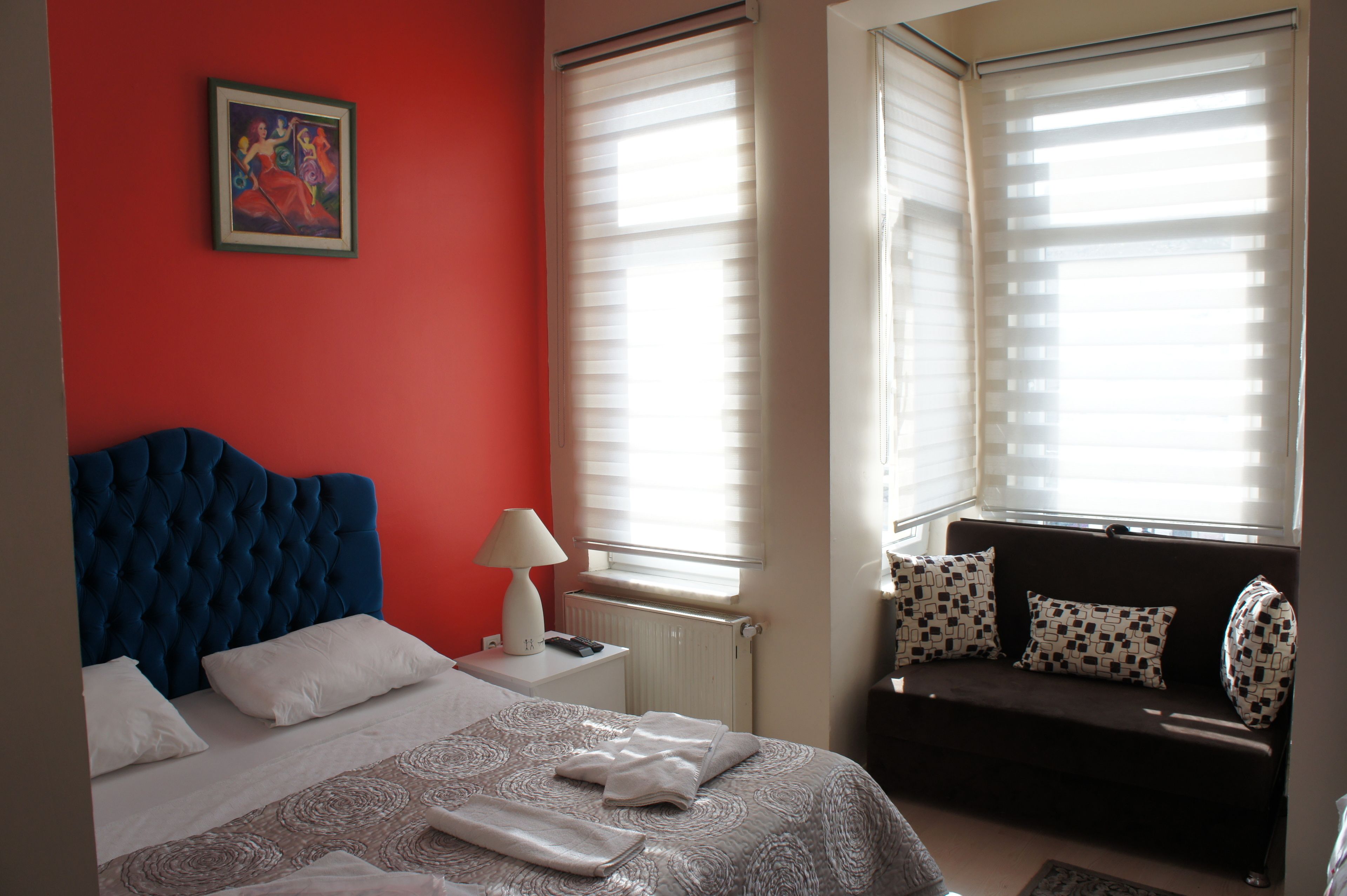 A hotel room with a blue headboard bed, a sofa with patterned cushions, and a painting on the wall.