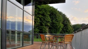 Una terraza moderna al aire libre con paredes de vidrio, mobiliario de mimbre y vistas a un bosque frondoso.