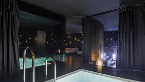 A modern indoor pool area with a glass partition, metal railings, and a view of the city at night. - Hotel Soho Boutique Granada (Granada)