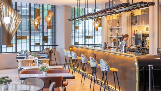 A modern restaurant interior with a bar area, high chairs, and a counter where a staff member is working. - Hotel Soho Boutique Granada (Granada)