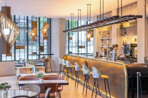 Interior moderno de restaurante con barra, sillas altas y mostrador donde trabaja un miembro del personal.